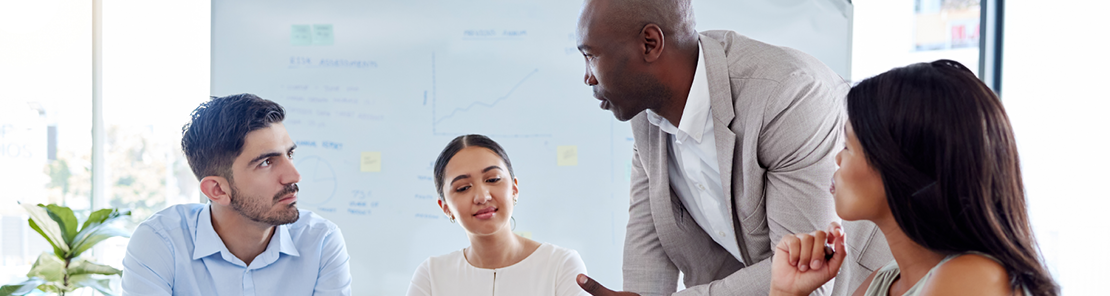  A group of business professionals sit at a conference table discussion business strategy and leadership objectives.