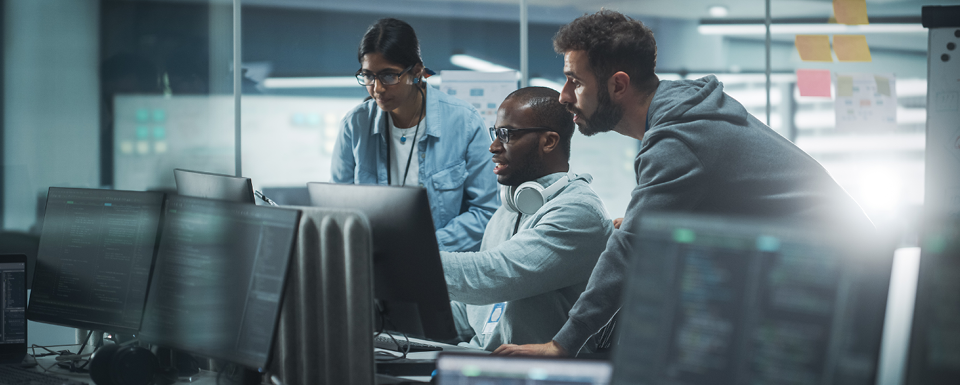 Three professional surrounded by computer screens review a cybersecurity plan.