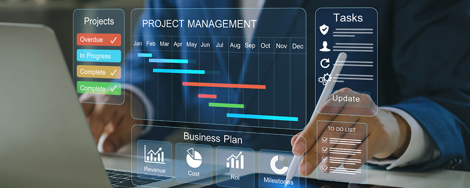 a reflection of a man is seen in a computer screen which displays the status of projects as well as projects over a monthly project management timeline and tasks.
